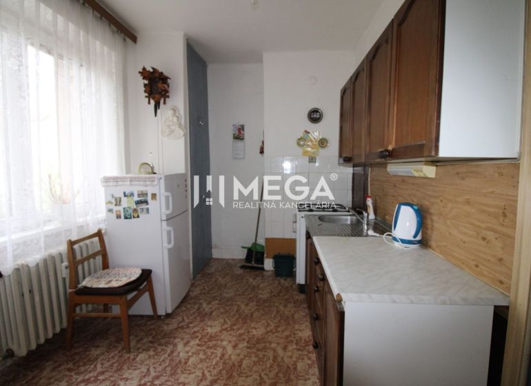 Kitchen in a 2-room apartment with a refrigerator, wooden decor flooring, light curtain.