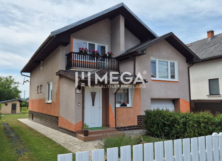 A family house in Lackovce with a balcony, surrounding greenery, and a white fence.