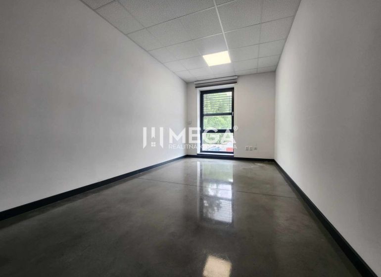 The interior of an office with a window, white walls, and a dark floor.