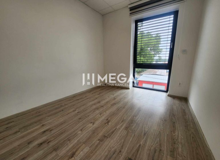 An office with a wood-patterned floor and a large window, simple interior.