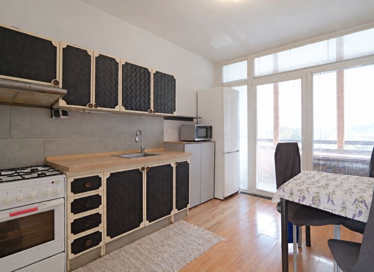 A kitchen in a 3-room apartment with a wooden decor floor and a dining area.