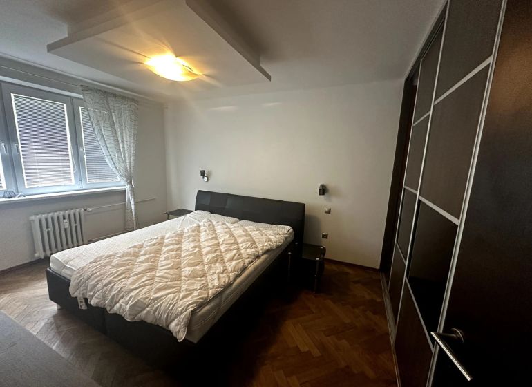 Bedroom in a two-room apartment with a bed, wardrobe, and wooden decor flooring.