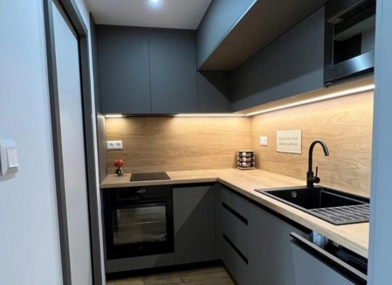 A kitchen in a studio apartment with a wood-patterned floor, gray cabinets, black sink.