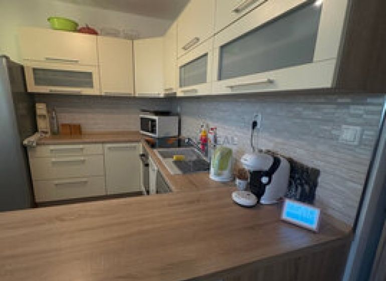 A kitchen in a 2-room apartment with a wooden decor floor and light furniture.