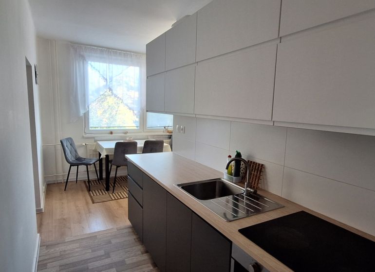 A kitchen in a 3-room apartment, with a wooden decor floor and a dining area.