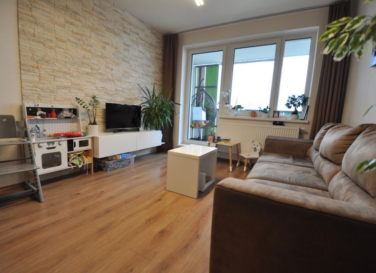 A living room in a three-room apartment with a wooden decor floor and stone cladding on the wall.