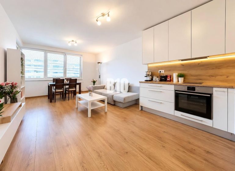 Living area with kitchen and wood-patterned flooring in a 2-room apartment.