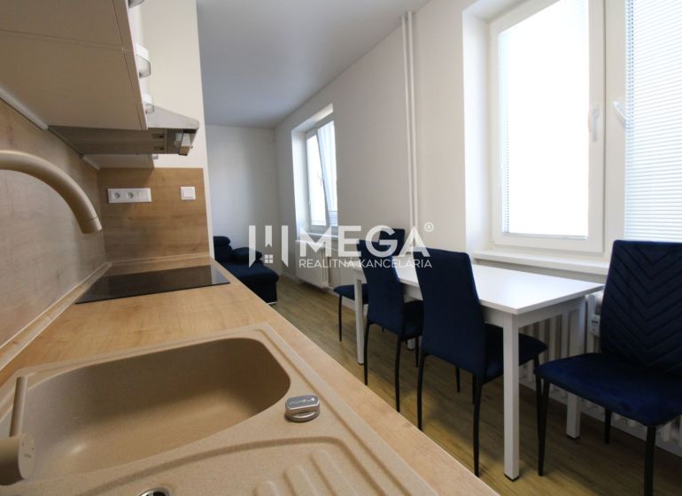 A kitchen in a 2-room apartment with white furniture, blue chairs, and a wooden-patterned floor.