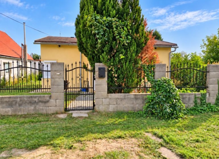 A family house in Martovce with a front garden and a metal gate, surrounded by a hedge.