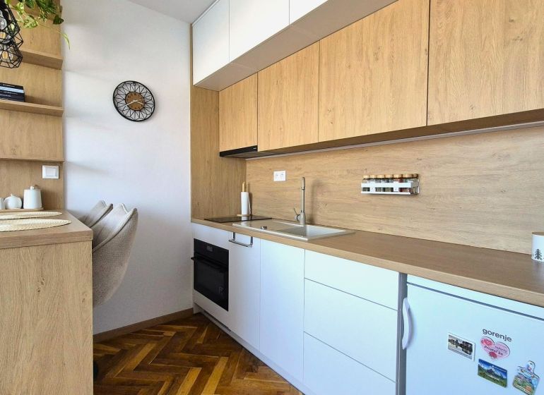 A kitchenette in a studio apartment with a wood-patterned floor and built-in appliances.