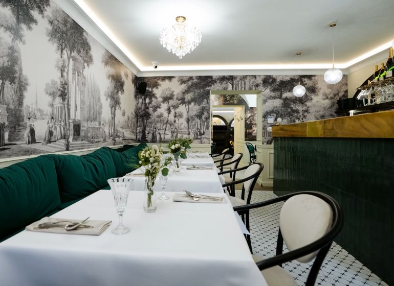 Interior with historical wallpaper, tables, green sofas, and a crystal chandelier in commercial premises.