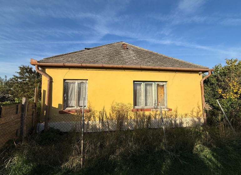 A yellow family house in Komárno with a fence and a garden under the blue sky.