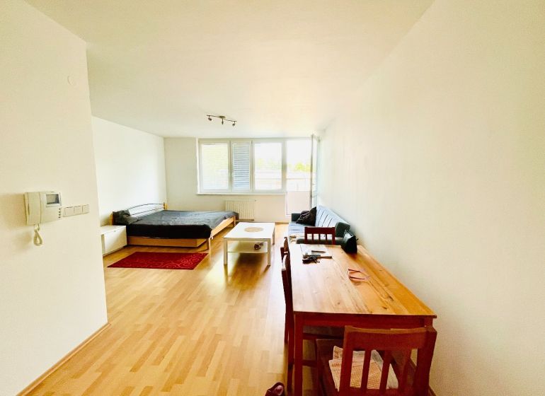 A one-room apartment with a wooden decor floor, with a bed and a work desk.