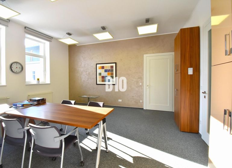 Interior of an office with carpeted floor, desk, chairs, and a wall painting.