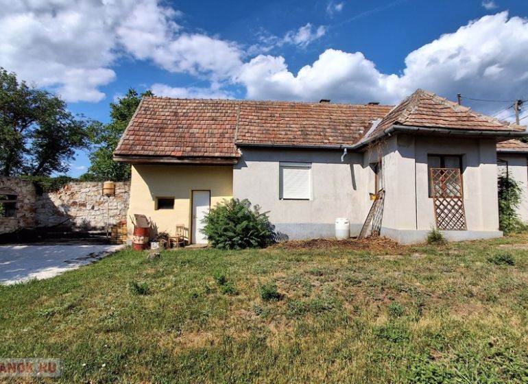A family house in Abaújkér surrounded by a garden and a stone wall under a blue sky.