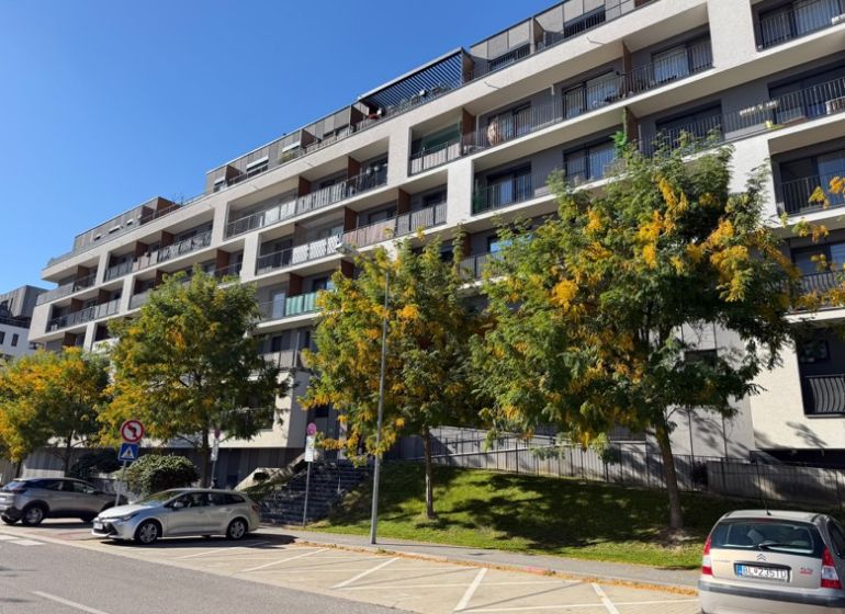 Apartment building in Bratislava-Petržalka with greenery and parking spaces in front of the entrance.