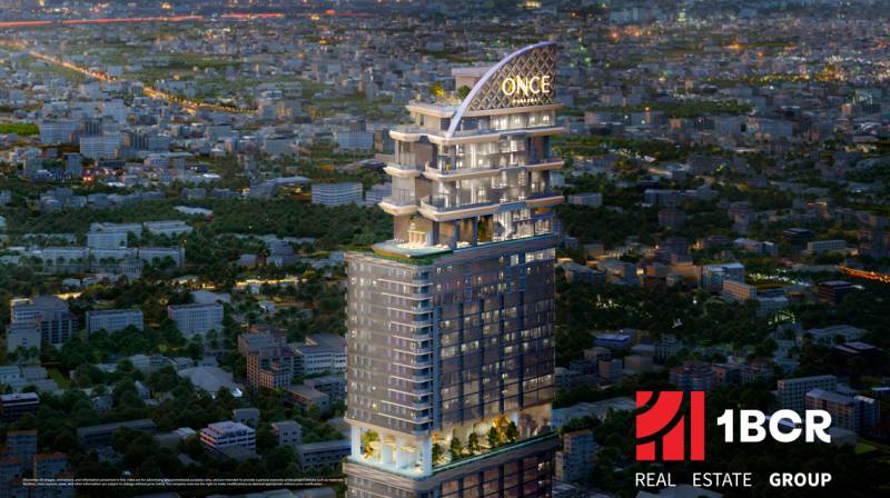 Apartment construction in Chon Buri 20150 with a bright skyscraper during the evening.