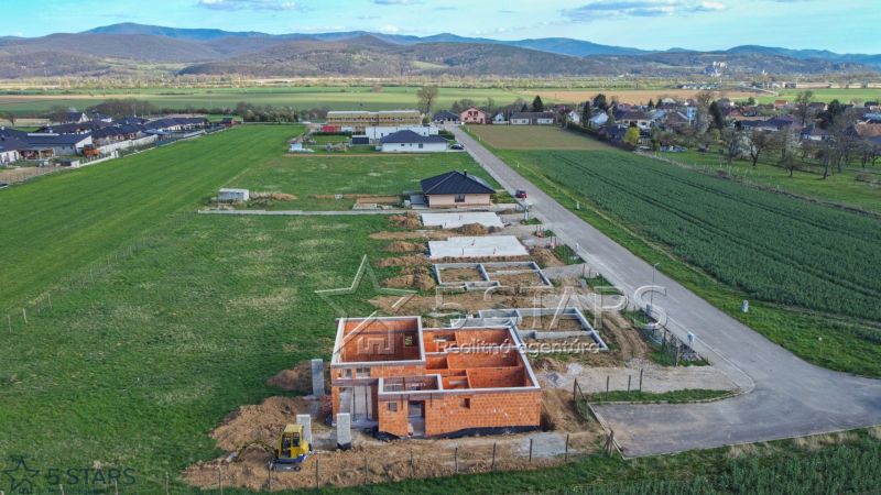 A construction project of a family house in Trenčín surrounded by green fields and a road.
