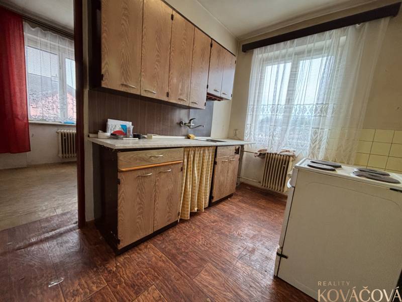 A kitchen in a 4-room apartment with older furniture, a window with white curtains.