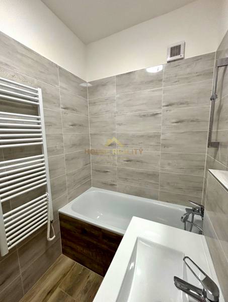 A bathroom in a 2-room apartment with a bathtub, a sink, and a ladder radiator.