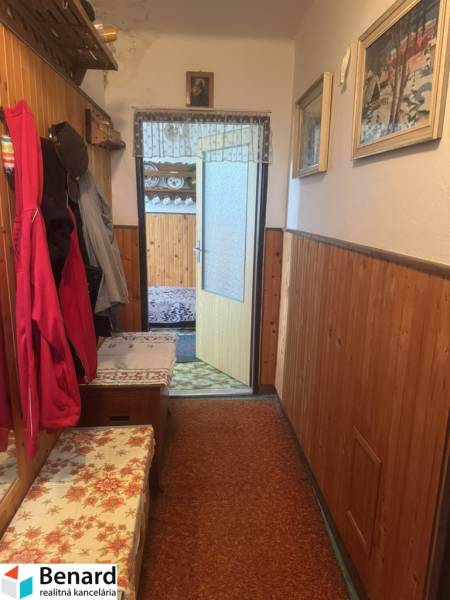 Hallway of a 2-room apartment with wooden paneling, coat hooks, and floral cushions.