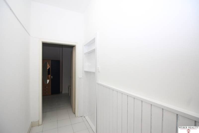 A white corridor leads to a room where a wardrobe with an oval mirror is visible.