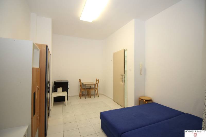 A simply furnished one-room apartment with a blue bed and a dining table.