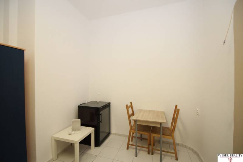 A simple interior in a studio apartment with a table, chairs, and a small refrigerator.