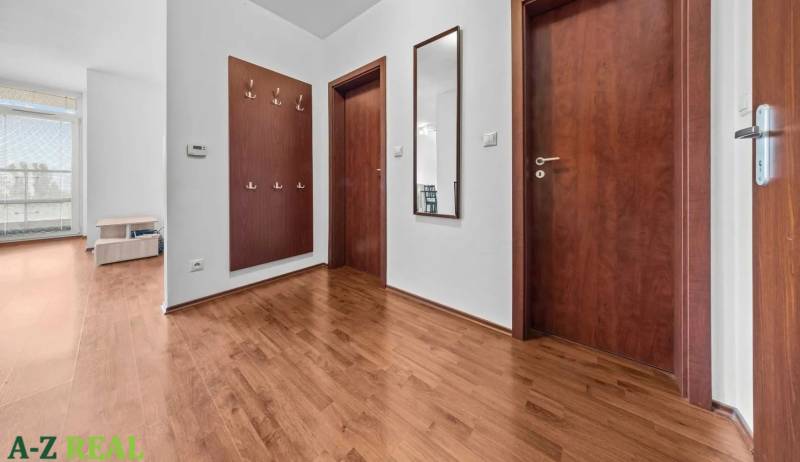A hallway with wooden doors and flooring, coat racks, and a mirror in a two-room apartment.