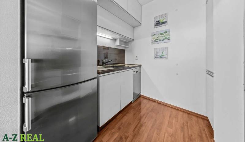 Kitchen area of a 2-room apartment with wooden flooring, a white kitchen unit, and a stainless steel refrigerator.