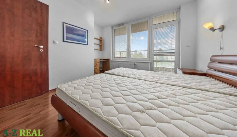 A bedroom in a two-room apartment with a large window, wooden furniture, and doors.