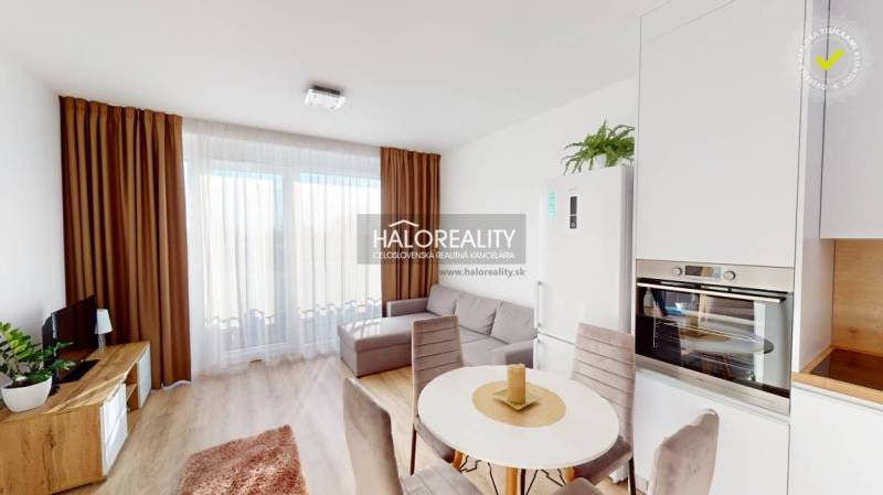 Living room in a two-room apartment with a sofa, dining table, curtains, and kitchen unit.