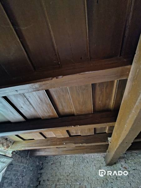 Ceiling of a rural family house with wooden beams and a stone wall.