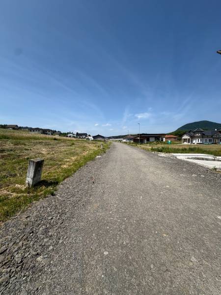 The road between residential plots in Gregorovce, with unfinished houses and mountains in the background.