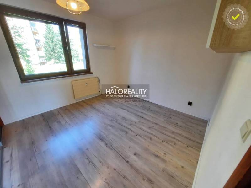 A room with a light floor in a 4-room apartment, large window, radiator, empty walls.