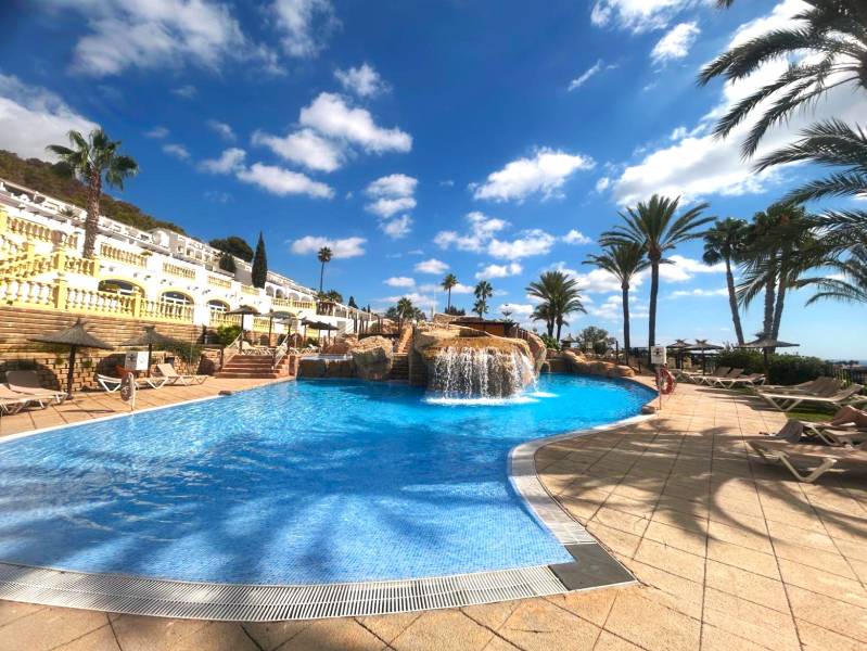 A pool with a waterfall surrounded by palm trees and loungers in a holiday apartment in Calpe.