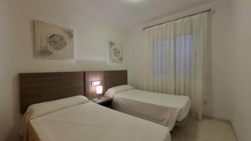 Two single beds, a nightstand with a lamp, and curtains in the vacation apartment.