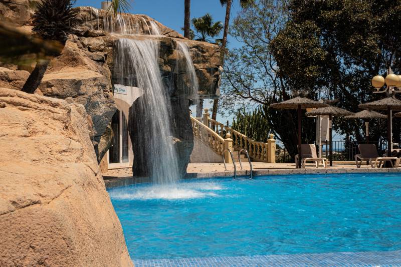 A pool with a waterfall and loungers in a holiday apartment in Calpe.