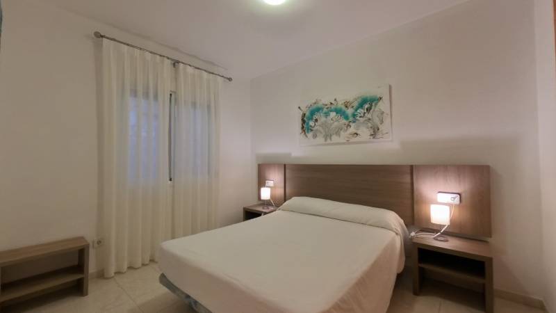 Bedroom in a holiday apartment with a double bed, wooden nightstands, and a painting.
