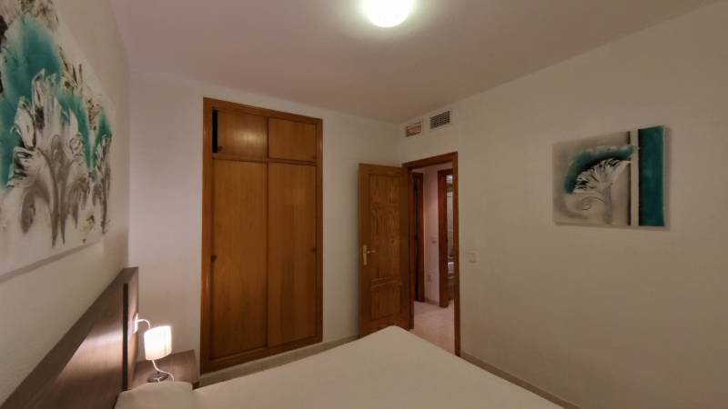 A bedroom in a holiday apartment with a bed, wardrobe, and decorative paintings on the walls.