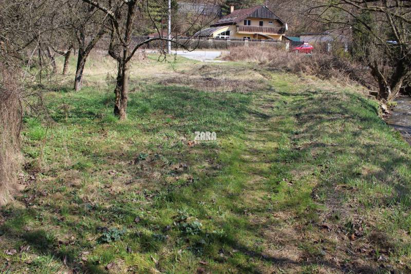 A grassy area near a stream with a house in the distance on Myslavská and Záhrady streets.