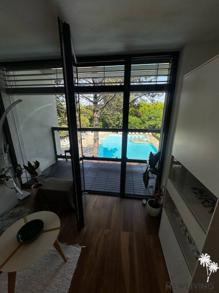 Interior of a 2-room apartment with a view of the pool and greenery through large windows.