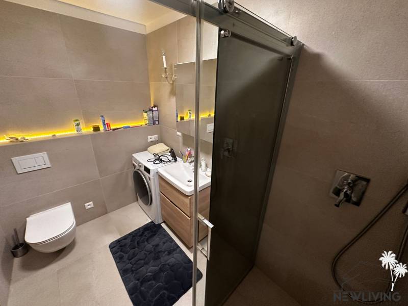 Bathroom in a 2-room apartment with a shower, washing machine, and toilet, with decorative lighting.