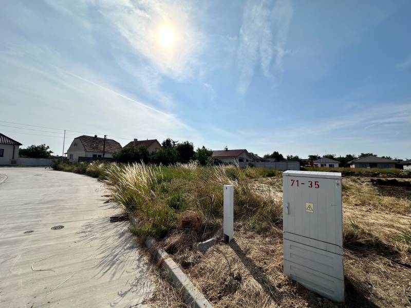 Plots - housing in Slovenská Nová Ves with a road and an electrical box on a sunny day.