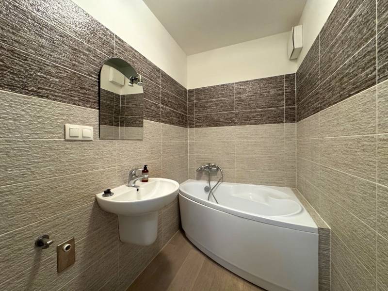 A bathroom with a corner bathtub and a sink in a 3-room apartment, surrounded by tiles.