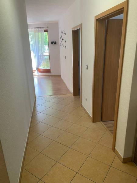 A hallway with tiles in a 3-room apartment, in the background a large window with a curtain.