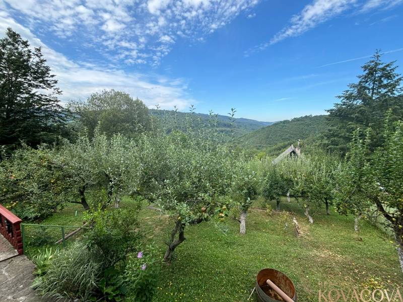 The picture shows fruit trees, hills, a cottage, and a blue sky.