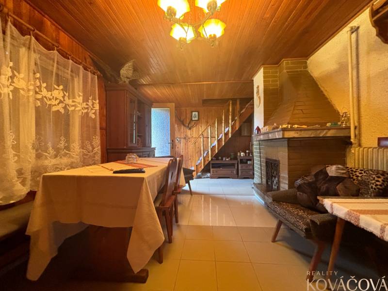 The interior of a wooden cabin with a fireplace, staircase, decorative curtains, and wooden furniture.