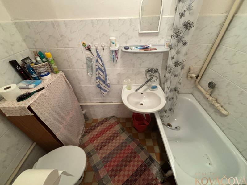 A small bathroom in a cottage with a bathtub, sink, mat, and curtain.