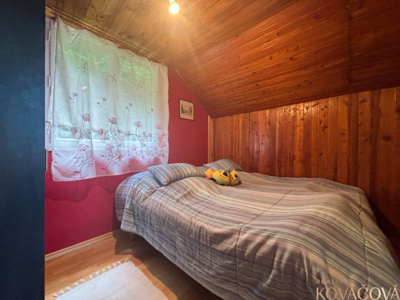 A bedroom in a wooden cabin with a double bed and a window with white curtains.